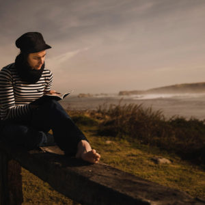Woman sitting on railing writing in a book while overlooking the ocean