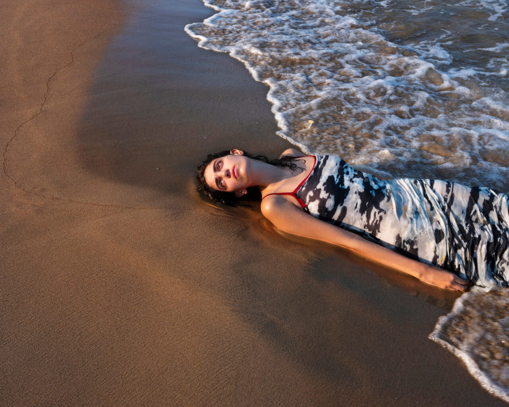 Rhea lying in the sand while the ocean washes over her