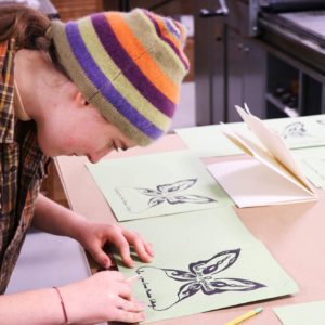 Book Arts & Design student focusing on their freshly printed letterpress design for a zine.