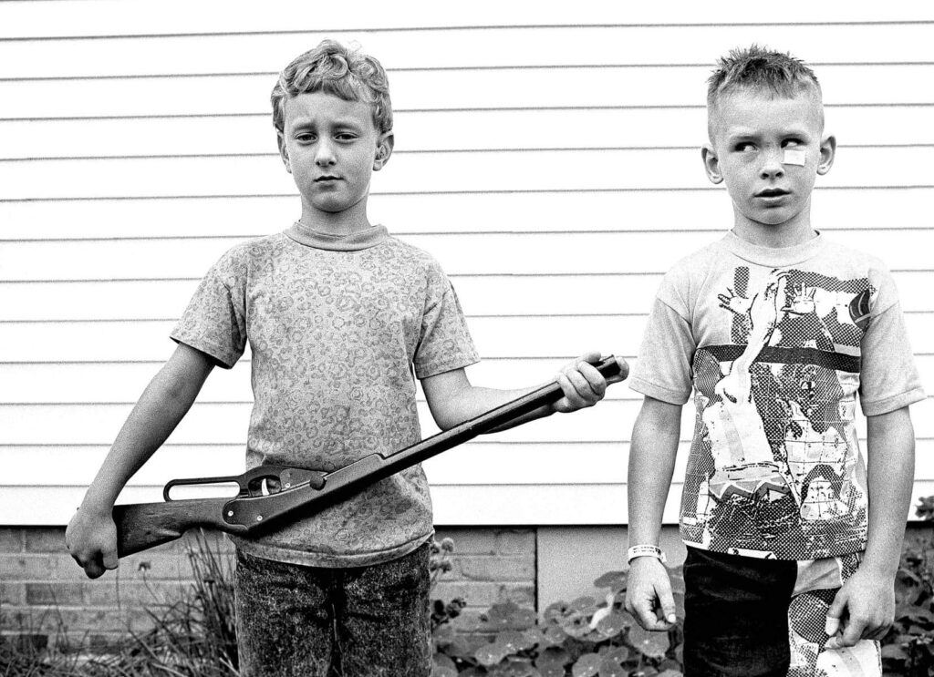 Two boys standing there with one of them holding a gun.