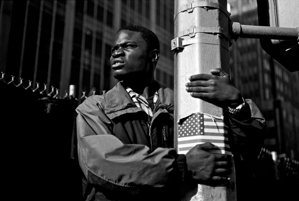 Photo by Steve Simon showing a black man holding on to a light pole.